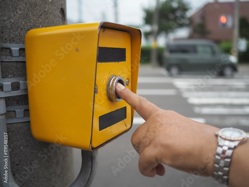 Hand pressing a button at traffic lights on pedestrian crossing.