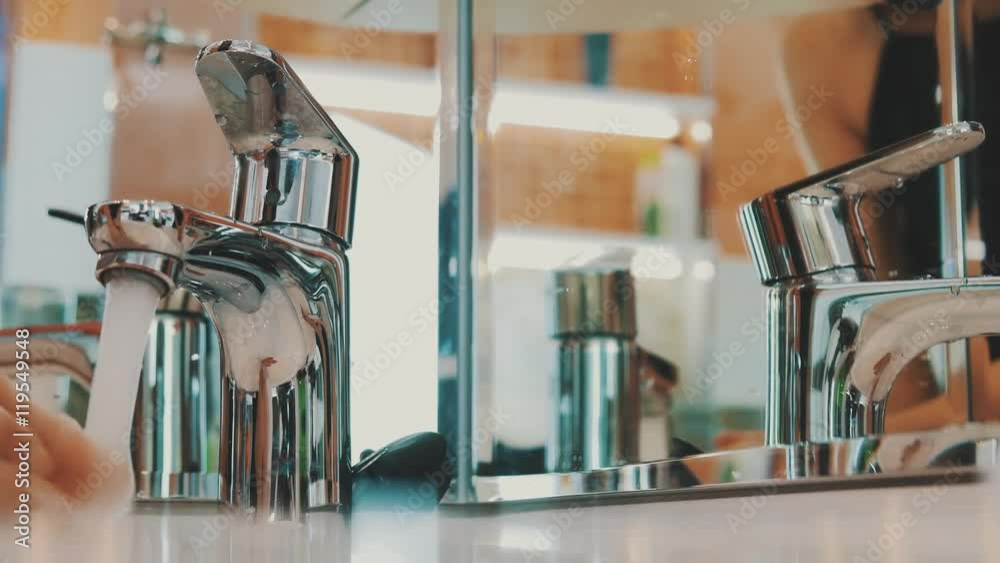 Young girl open faucet of sink in front mirror in bathroom. Water. Morning. Reflection