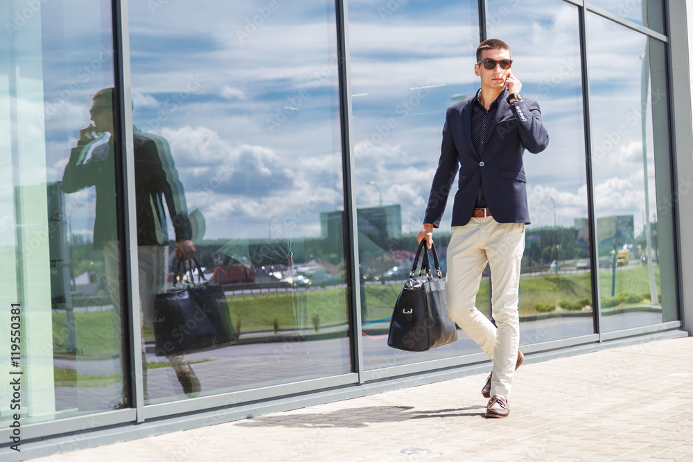 Elegant businessman call on mobile phone while walking with suitcase outside airport Elegant businessman call on mobile phone while walking with suitcase outside airport
