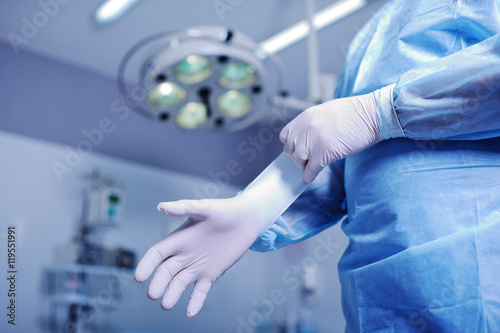Surgeon putting on sterile rubber gloves to complicated surgical operation on the background lights. Surgery photo