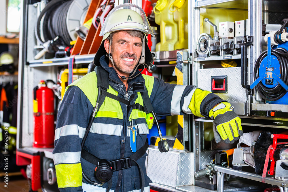Fototapeta premium Strażak w mundurze opiera się o samochód straży pożarnej