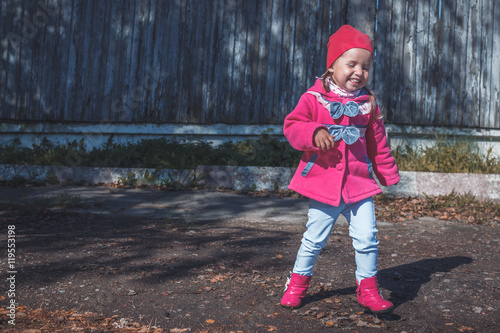 Little girl in a pink coat, jeans and boots walking the park