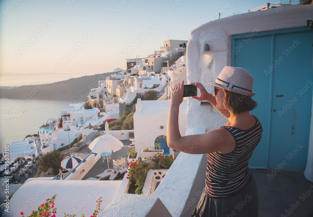 Obraz premium young woman tourist taking photo on mobile phone smartphone in Greece Santorini at sunset