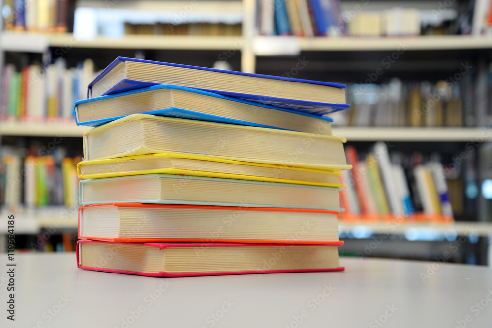 Close up of colorful books on the table. Bookshelves in the background. Close up of colorful books on the table. Bookshelves in the background.