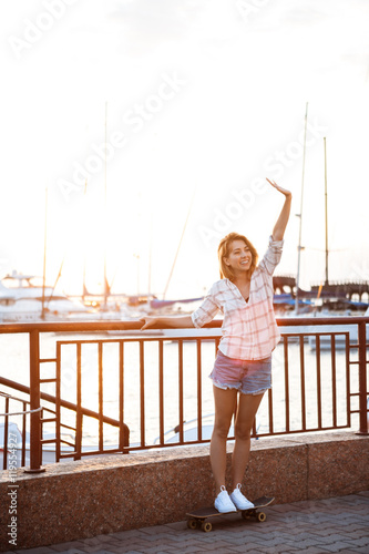 Fototapeta Naklejka Na Ścianę i Meble -  Young beautiful girl walking at seaside, smiling, greeting, skateboarding.