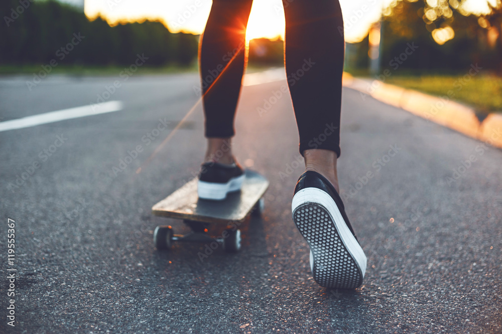young skateboarder legs riding on skateboard in front of the sun