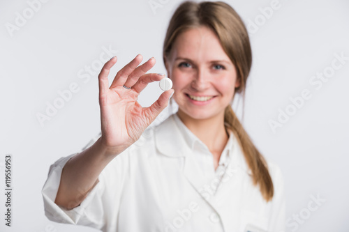 Doctor woman showing pill. Young female medical professional isolated on white background. Selective focus.