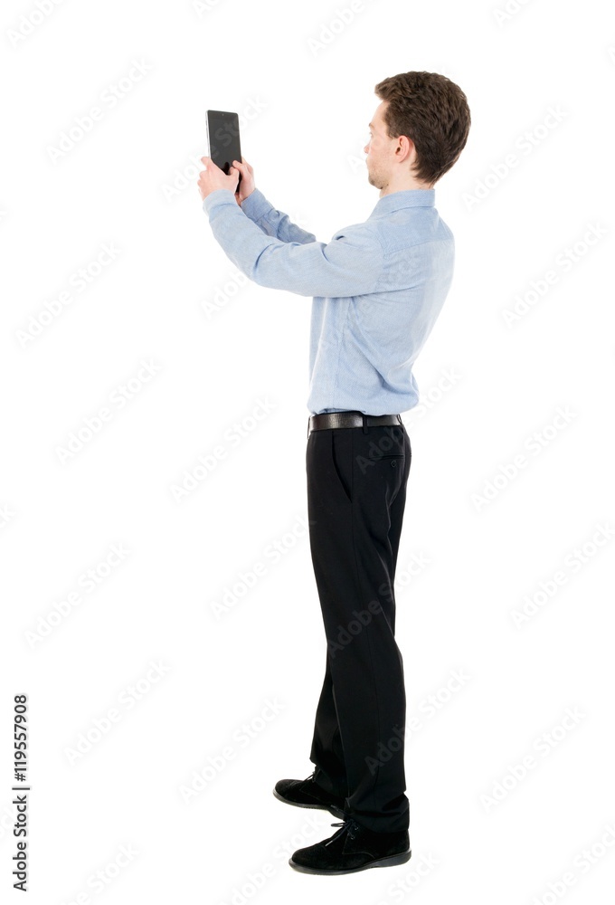 back view of standing business man photographing a phone or tablet. curly-haired businessman in light shirt photographed on a Tablet PC. back view of standing business man photographing a phone or tablet. curly-haired businessman in light shirt photographed on a Tablet PC.