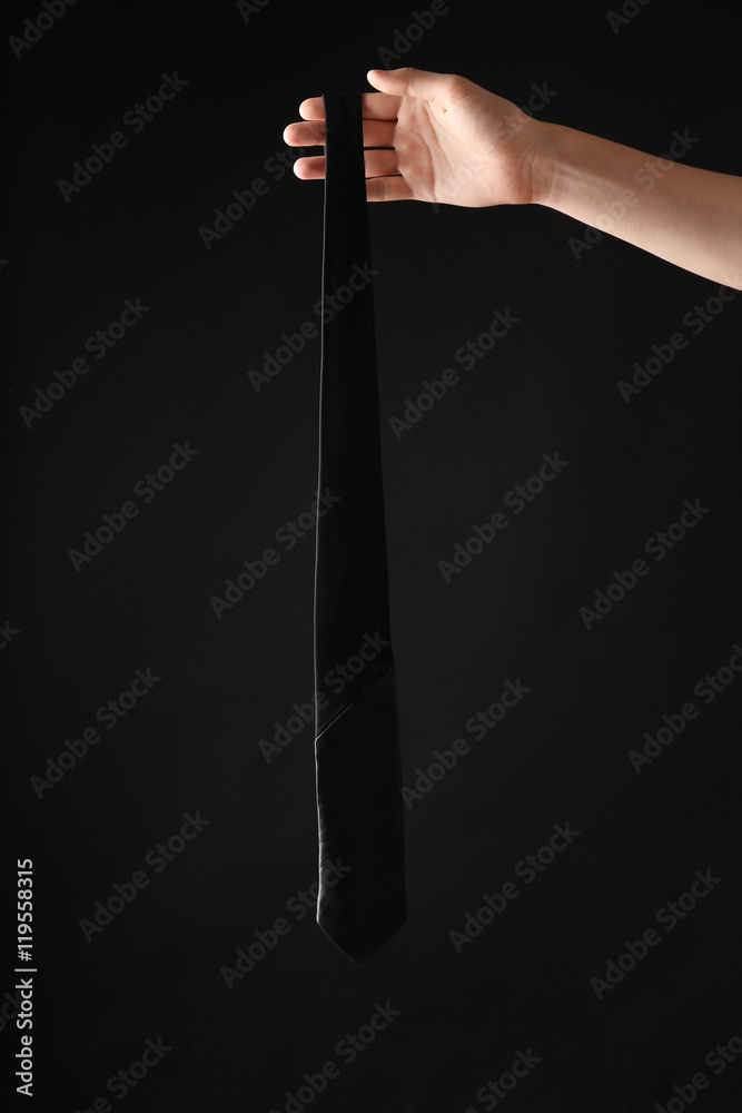 Female hand holding black tie on dark background
