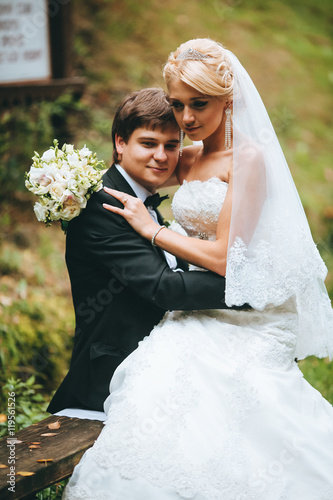 Glad newlyweds stand on fallen leaves in autumn park. Froom kissing bride. Green and red forest. photo