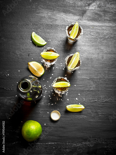 bottle of tequila with shot glasses, fresh lime and salt.
