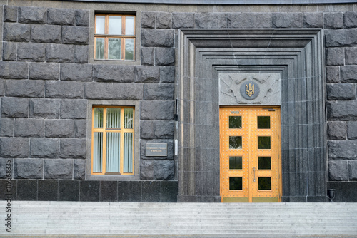 Entrance to the Government House of Ukraine. The coat of arms of Ukraine is above the door. Inscription on the board beside the entrance states this is the Government House of Ukraine. © olenaari