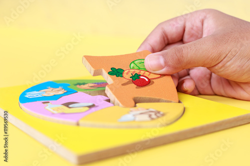Hand of kid holding wooden jigsaw of the 5 food Groups. Child de
