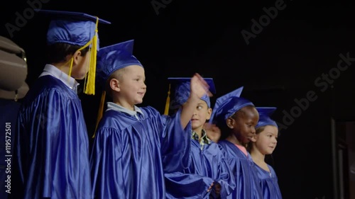 Small young graduation class on stage and waving