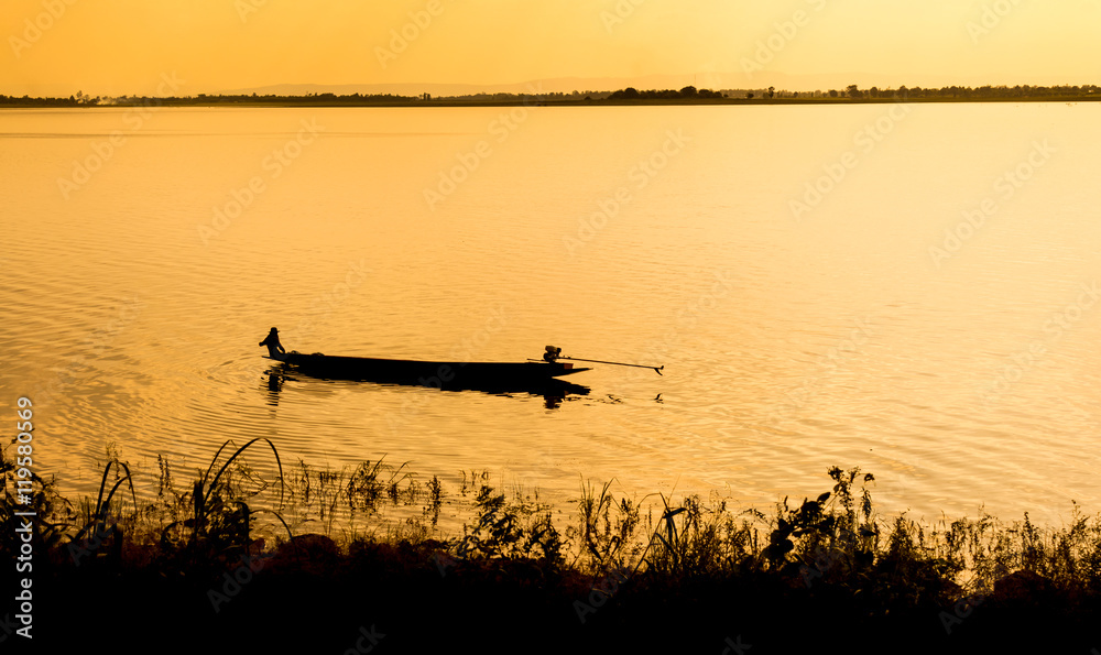 A lone fisherman moves out on a lake in a small boat as the sun