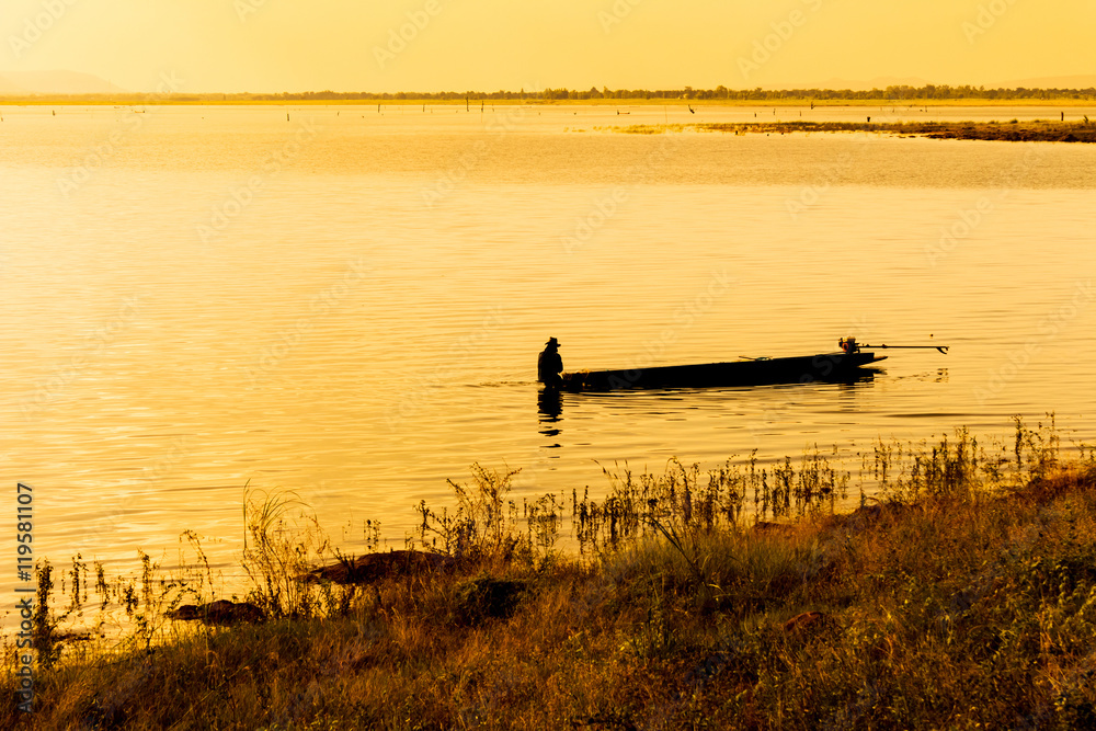 A lone fisherman moves out on a lake in a small boat as the sun