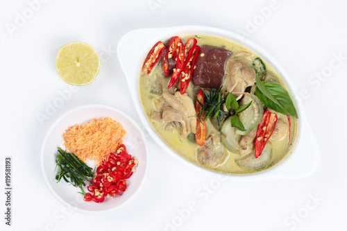 Green chicken curry in coconut milk served with side dish as minced dried shrimp,sliced red chili,sliced kaffir lime leaves and green lemon on white background.