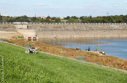 group of fishermen on the bank of a drying dam with revealed bottom covered with colorful plants in autumn photo