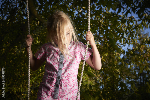 Child blond sad girl standing on swing.