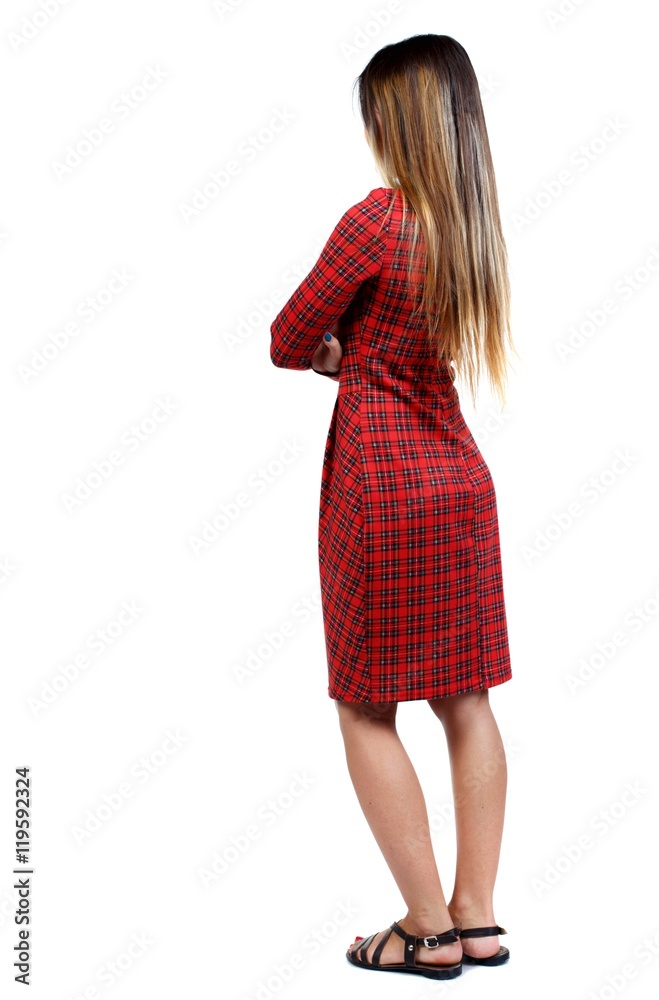 back view of standing young beautiful woman. girl in red plaid dress standing sideways with his arms crossed. back view of standing young beautiful woman. girl in red plaid dress standing sideways with his arms crossed.