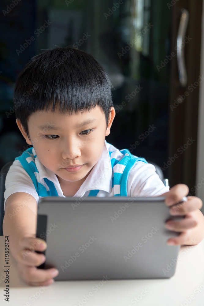 Young asian boy sitting , he browses the internet on a tablet computer at home. Young asian boy sitting , he browses the internet on a tablet computer at home.