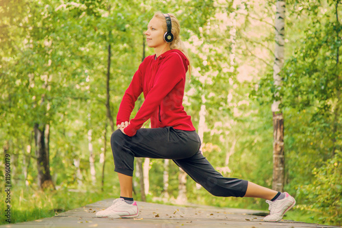 Young woman gymnastics in the park on trail and listening music in summer fresh air early morning.