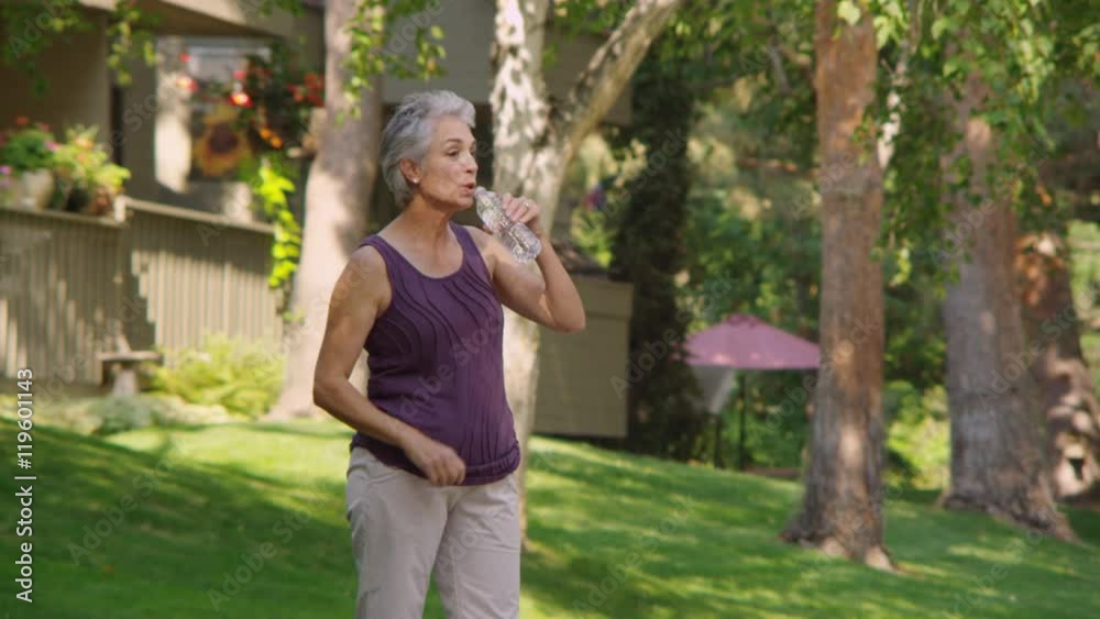 Elderly woman drinking water and sitting near stream Elderly woman drinking water and sitting near stream