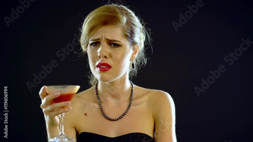 Girl drinking martini and crying. Girl dressed in an evening dress. Black background. 4k.