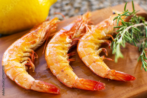 Grilled Shrimps Served on a Wooden Plate With Lemon and Rosemary. Three Grilled Seasoned Shrimps Closeup.