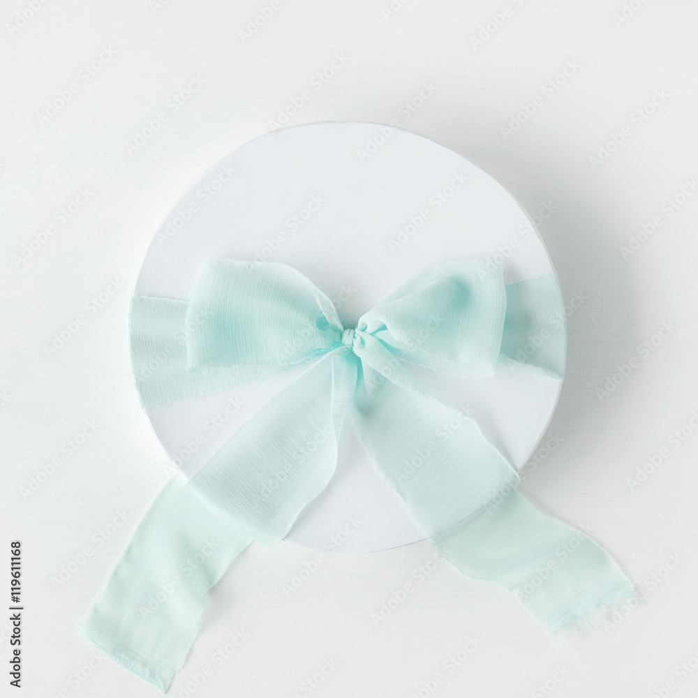 Naklejka premium white gift cardboard box with blue bow on white background. flat lat, top view