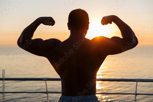 Silhouette of muscular showing biceps at sunnrise photo