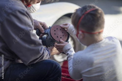 Senior man and boy looking at grinding machine at car photo