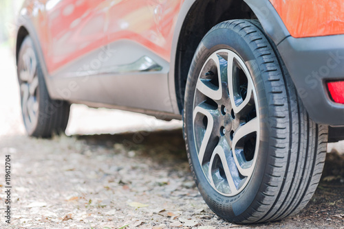 Close up of car tyres. Back view of a parked car over a road covered with autumn leaves.