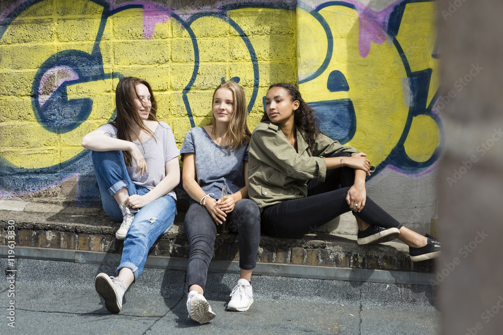 Three teenage girls relaxing on roof top in front of graffiti