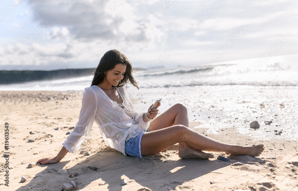 Spain, Asturias, beautiful young woman with smartphone on the beach Spain, Asturias, beautiful young woman with smartphone on the beach