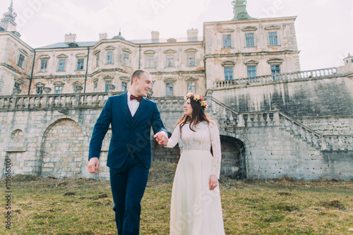 Charming newlywed bride and groom walking near beautiful ruined baroque palace