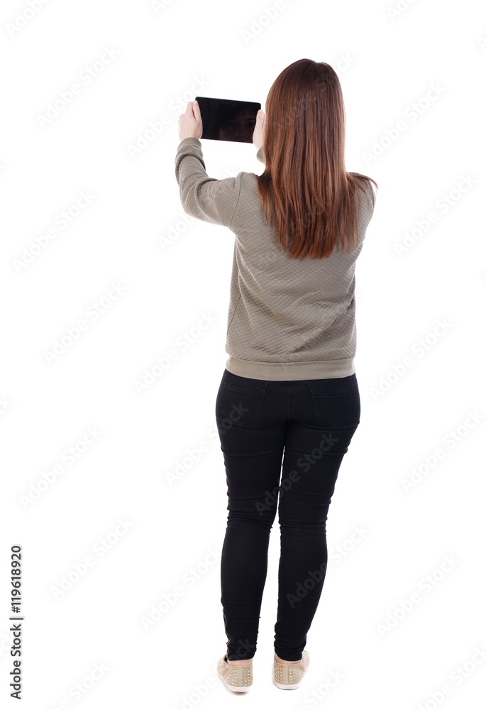 back view of standing young beautiful woman using a mobile phone. girl watching. A girl in a gray sweater holds a tablet on outstretched arms. back view of standing young beautiful woman using a mobile phone. girl watching. A girl in a gray sweater holds a tablet on outstretched arms.