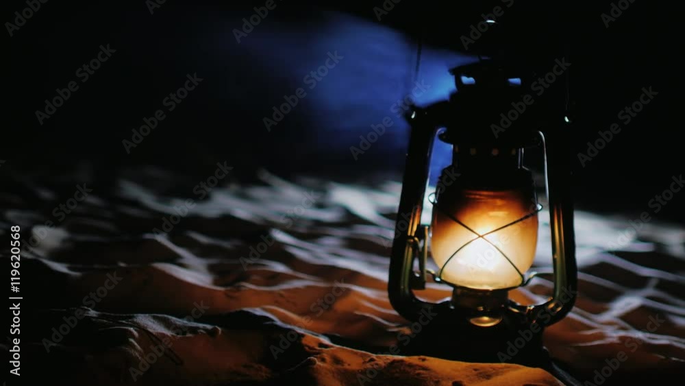 Old kerosene lamp shines. It stands on the sand at the beach in the dark. Beautiful blue smoke comes from the top