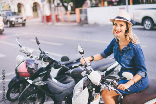 Outdoor portrait of pretty young woman with red lips make-up in hat sitting on scooter.