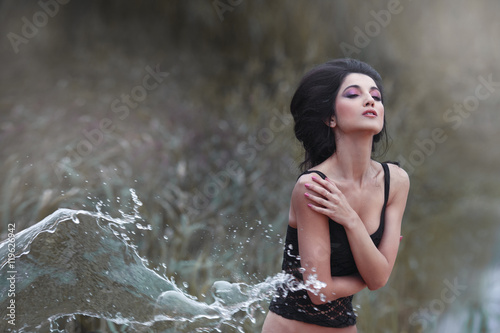 Beautiful brunette in a spray of water outdoors.