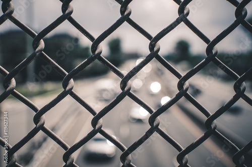 Image of chain link fence on bridge over pass. Chain fence on bridge above highway. Abstract industrial image of chain link fence and cars on highway.