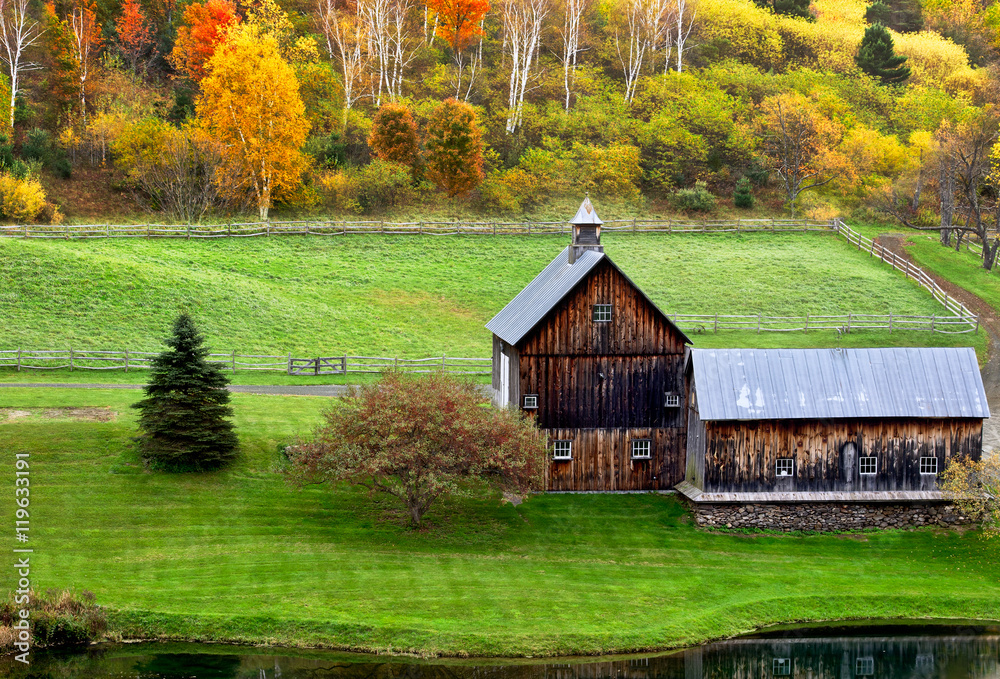 Fototapeta premium Beautiful old barn in a green meadow and colorful autumn trees