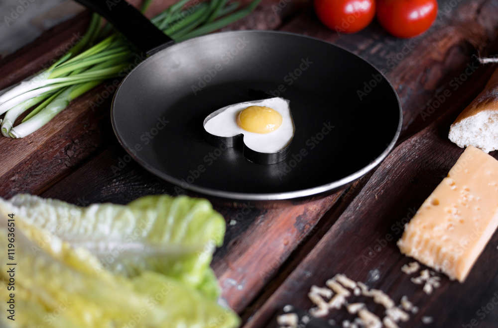 Fried eggs on a frying pan with different ingridients around on a wooden background