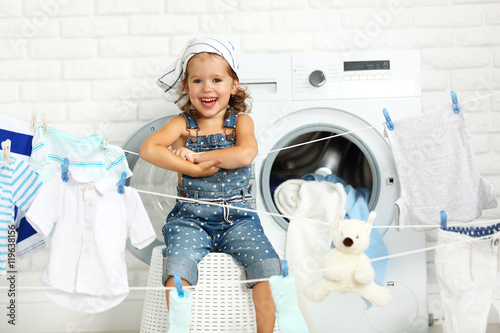 child fun happy little girl  to wash clothes and laughs in laund photo