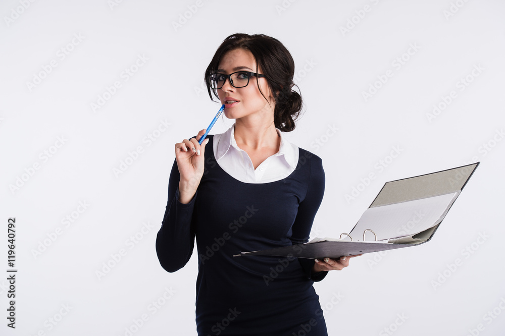 Young Caucasian woman wearing dark blue dress, white shirt, holding a ring binder folder and pen. Isolated on light background. Young Caucasian woman wearing dark blue dress, white shirt, holding a ring binder folder and pen. Isolated on light background.