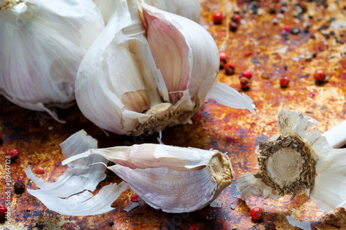 Garlic cloves on a warm textured metallic background with scattered pepper corns photo