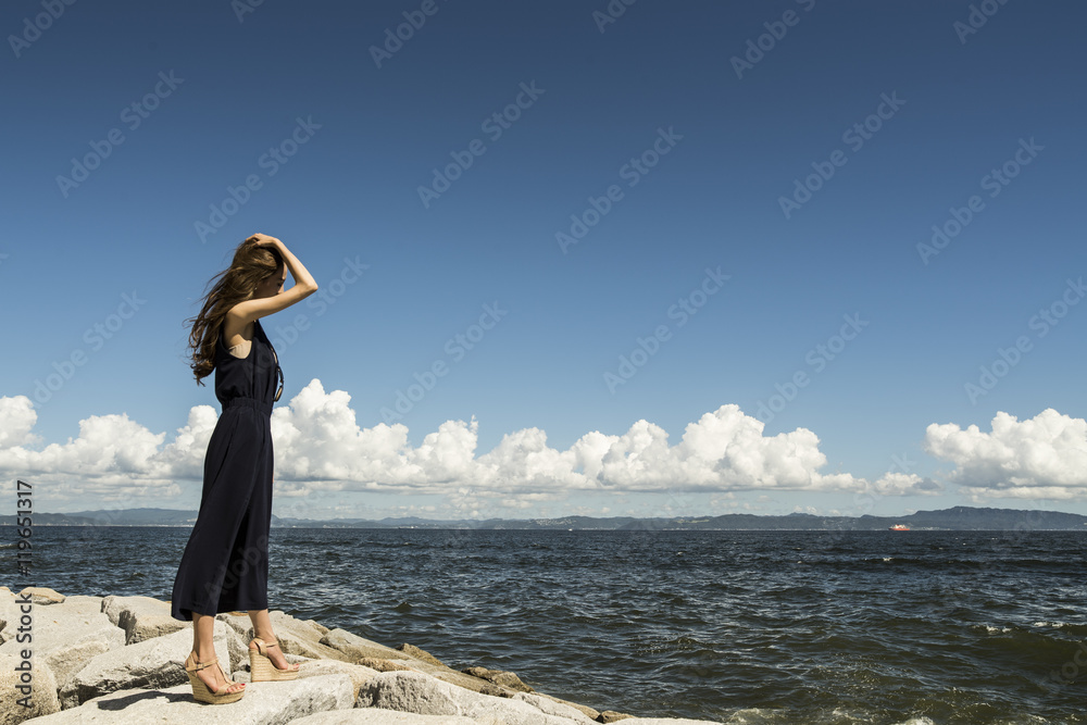 Young women are looking at the ocean standing on the rocks Young women are looking at the ocean standing on the rocks