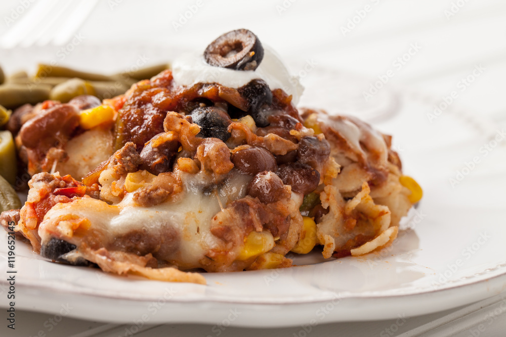 Fiesta bake Mexican lasagna with corn tortillas, pinto beans, olives, corn, tomatoes, and sour cream served with green beans close up shot Fiesta bake Mexican lasagna with corn tortillas, pinto beans, olives, corn, tomatoes, and sour cream served with green beans close up shot