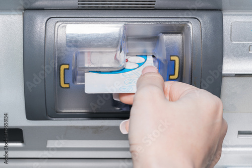 Hand inserting ATM card into bank machine to withdraw money 