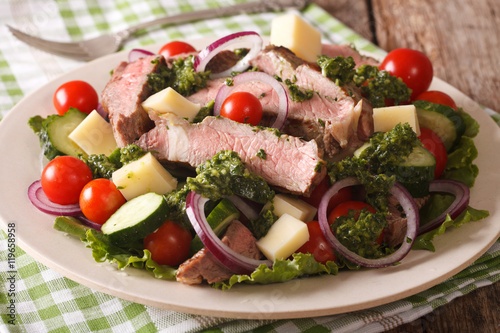 Tasty salad with beef steak, cheese and vegetables with green sauce closeup. horizontal 